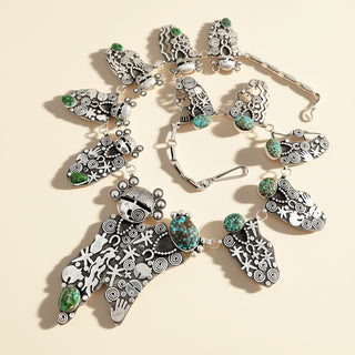 Silver necklace with intricate designs and green gemstones on a beige background