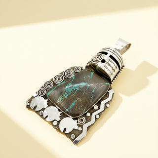 Black and turquoise warrior pendant with intricate designs on a beige background