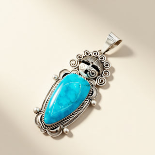 Turquoise pendant with silver intricate design on a beige background