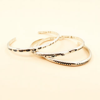 Three silver bangles on a beige background
