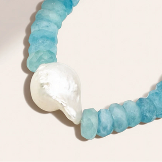Blue beaded bracelet with a large white pearl on a light background