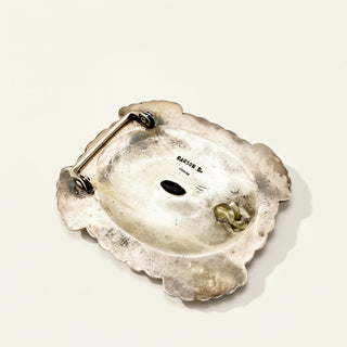 Silver brooch with scalloped edge and floral design on a white background