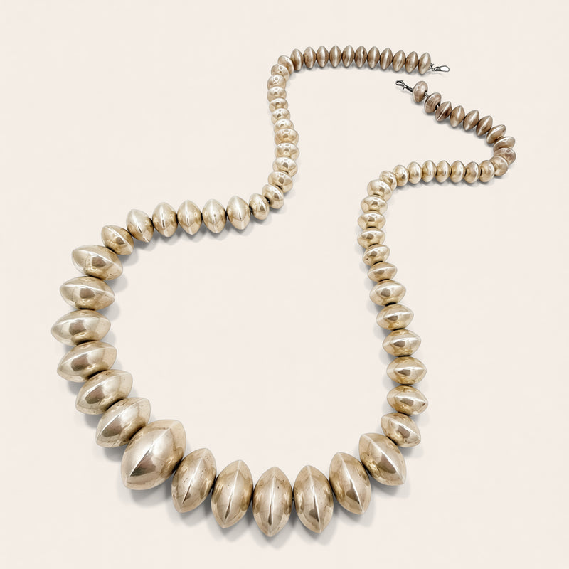 A chunky statement necklace made of matching beaded chain and clasp visible at the top right, set against a solid off-white background.