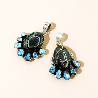 Pair of earrings with dark central stones and turquoise accents on a beige background