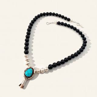 Necklace with black beads, turquoise stone, and silver clasp on a white background