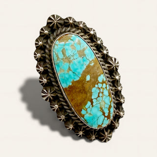 Turquoise stone in a decorative metal setting on a light gray background