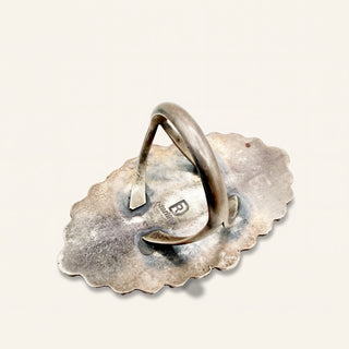 Silver ring on a matching silver dish with 'R' logo on a light gray background