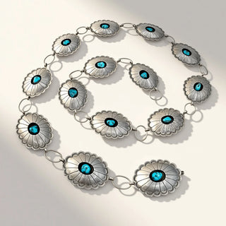 A sterling silver chain bracelet featuring multiple scalloped flower-shaped medallions, each set with a vibrant turquoise stone in the center, arranged in a loose spiral on a light beige background with soft shadows.
