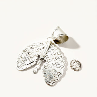 A sterling silver pendant featuring a textured, wavy pattern and a small attached coin charm, displayed on a clean off-white background next to a coin for scale.
