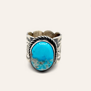 A sterling silver cuff ring featuring a large oval turquoise cabochon stone with natural matrix inclusions, set against a plain off-white background.