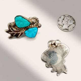 Turquoise stone brooch, silver leaf-shaped pendant, and U.S. quarter on a reflective surface