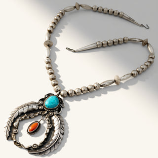 A silver-toned Southwestern-style necklace featuring a large circular pendant with a turquoise stone and an orange stone, accented with scalloped details and a beaded chain.