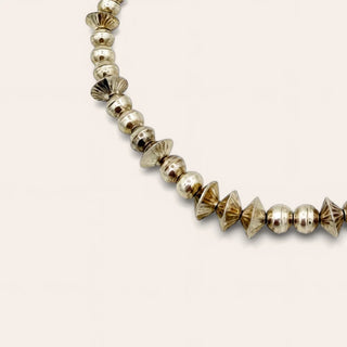 A beaded necklace ncluding textured cone-shaped beads and small heart-shaped beads, arranged in a circle on a light beige background.