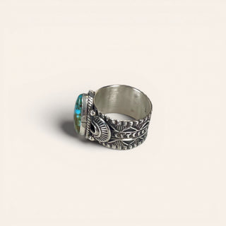 Silver ring with intricate designs and a central gemstone on a light beige background