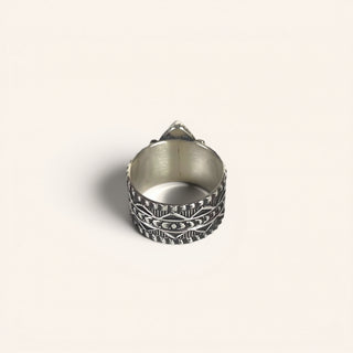 Silver ring with intricate design on a beige background