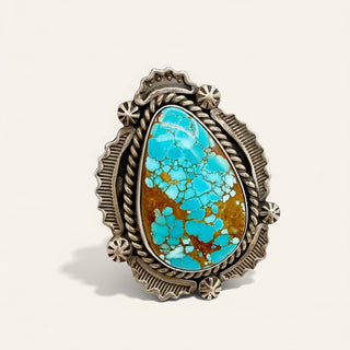 Turquoise stone ring with ornate silver band on a beige background