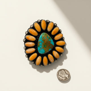 Jewelry piece with orange stones and a central turquoise stone on a light background