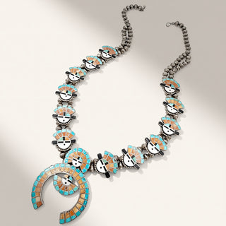 A Southwestern-style turquoise and silver necklace featuring a large spiral pendant and multiple  face inlays, displayed on a light beige background.