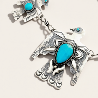 Multiple silver birds with turquoise stones on a handmade chain sitting on a cream background