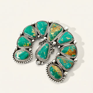 A sterling silver pendant featuring multiple green turquoise stones with natural gold and brown matrix patterns, set against a light beige background.