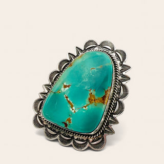 Turquoise stone ring with silver decorative band on a light beige background