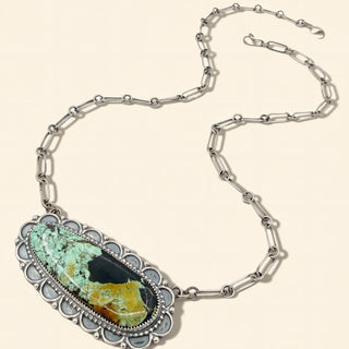 Necklace with a large pendant featuring a green and brown stone on a beige background