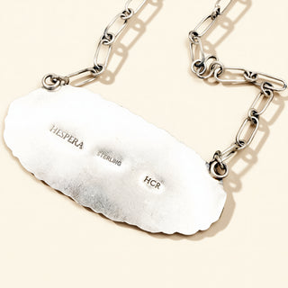 Silver necklace with a textured pendant on a beige background