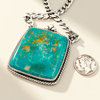 Turquoise pendant on a silver chain with a coin for scale on a light background