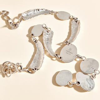 Silver stamp of necklace with 'Hespera' on a beige background