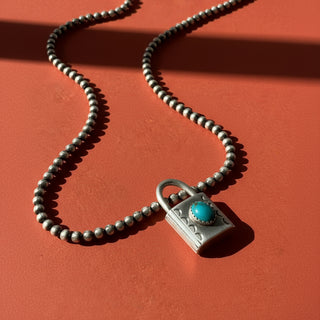 Silver lock charm with turquoise stone on and beaded chain on and orange surface