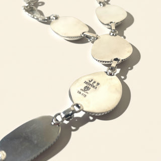Necklace with white circular pendants and silver clasps on a beige background