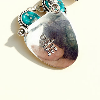 Pendant with turquoise stones and engraved text on a white background
