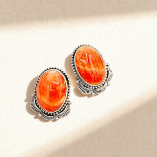 Pair of earrings with orange stones and silver frames on a beige background