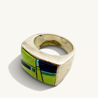 Silver ring with green and blue stone on a beige background