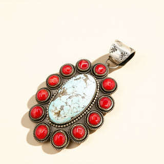 Jewelry pendant with turquoise stone and red accents on a beige background