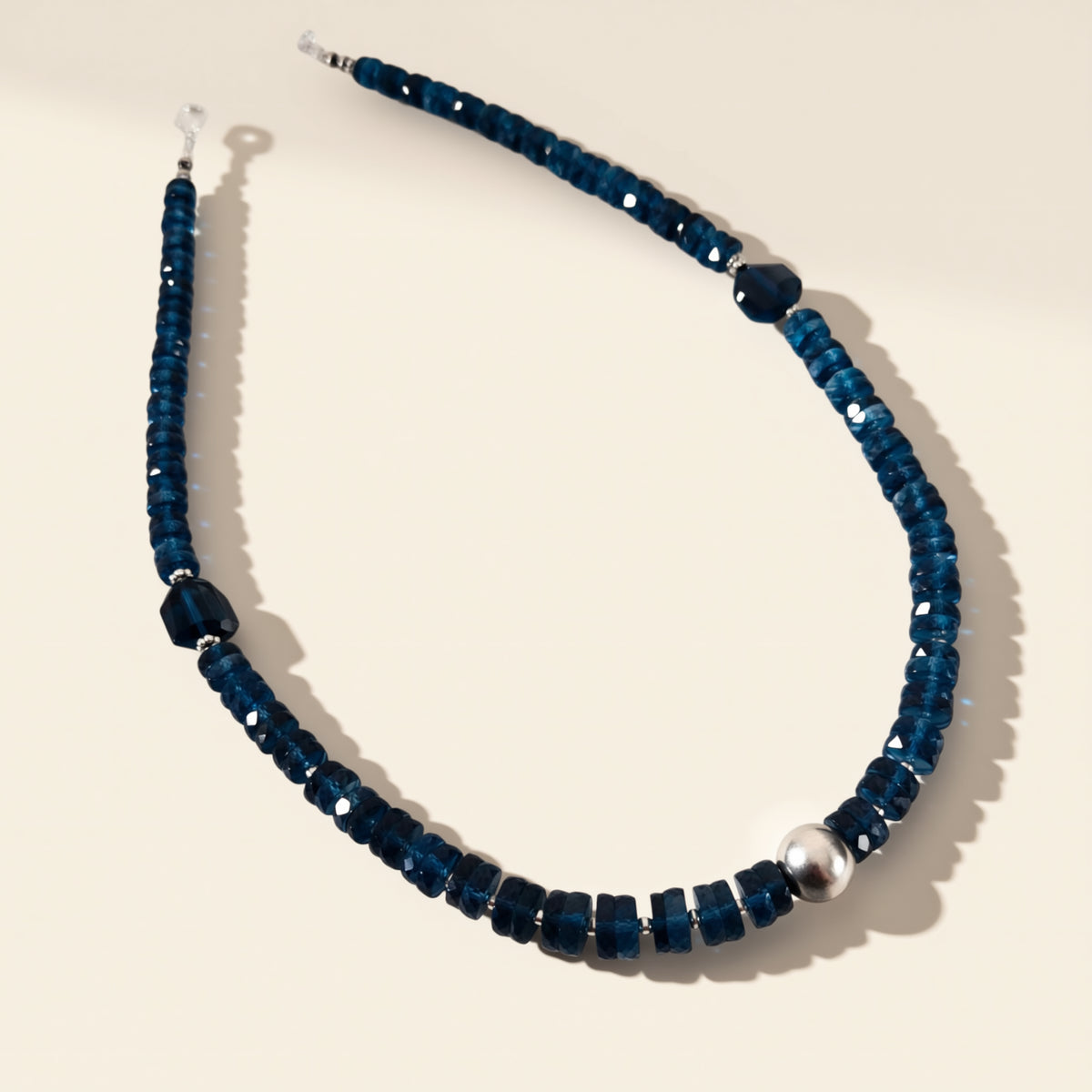 Blue beaded necklace with a silver clasp on a beige background