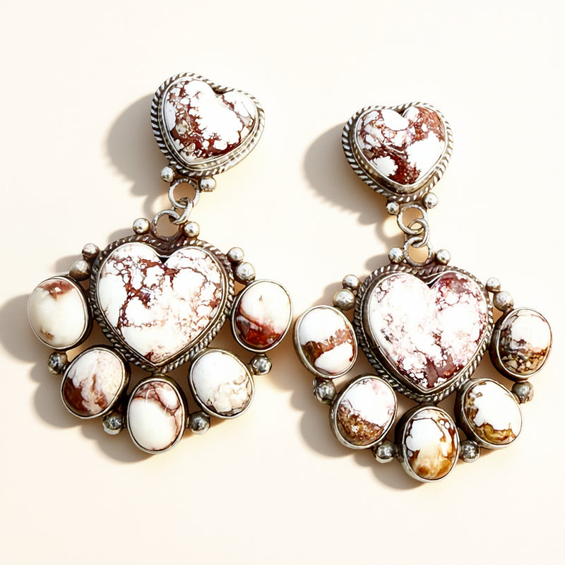 Pair of earrings with heart-shaped and round stone designs on a light background