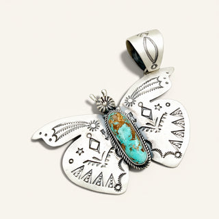 A Southwestern-style sterling silver butterfly pendant featuring a central turquoise stone with brown matrix, set against a light beige background.
