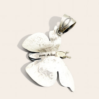 A textured sterling silver butterfly pendant with a bail, featuring engraved details and a small heart charm, shown on a light beige background.