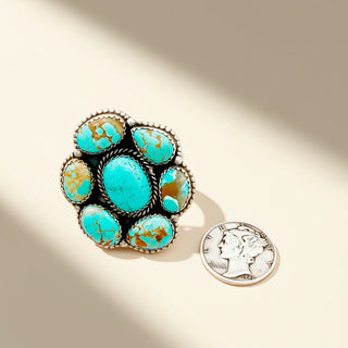 Turquoise ring with silver accents next to a U.S. quarter on a beige background