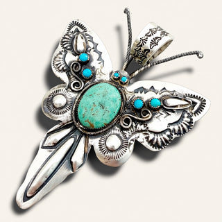 silver butterfly pendant with turquoise stones on a beige background