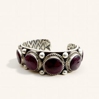 A sterling silver cuff bracelet featuring five round, deep burgundy gemstones, set in a traditional Southwestern style with textured bezels and small silver beads, photographed on a light cream background.