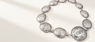 A silver-toned concho-style bracelet with multiple oval engraved medallions connected by small links, photographed on a clean white background.