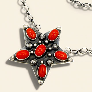 Star-shaped pendant with red stones and silver accents on a chain against a light background