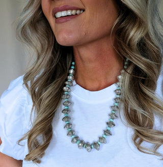 Woman wearing a white shirt and a green beaded necklace with a blurred background