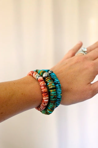 Hand wearing colorful beaded bracelets on a plain background