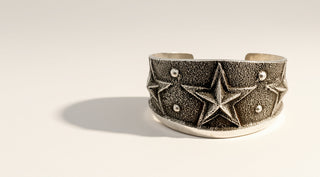 A textured sterling silver cuff bracelet featuring embossed star designs and small round silver bead accents, displayed on a clean off-white background with a soft shadow.