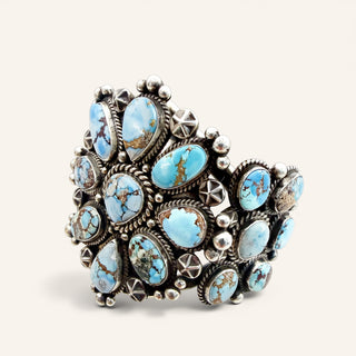 A wide silver cuff bracelet adorned with multiple oval turquoise stones in light blue and brown tones, set in detailed sterling silver bezel settings against a light beige background.