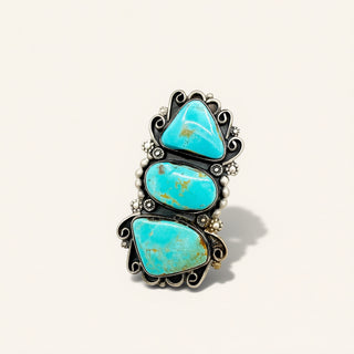 A silver ring featuring three stacked, scalloped turquoise cabochon stones with natural matrix inclusions, accented with small white beads, on a light beige background.