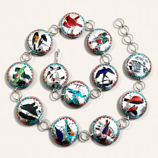 A silver link bracelet featuring twelve oval cabochon charms, each decorated with a different colorful bird illustration on a white background with turquoise and red borders.
